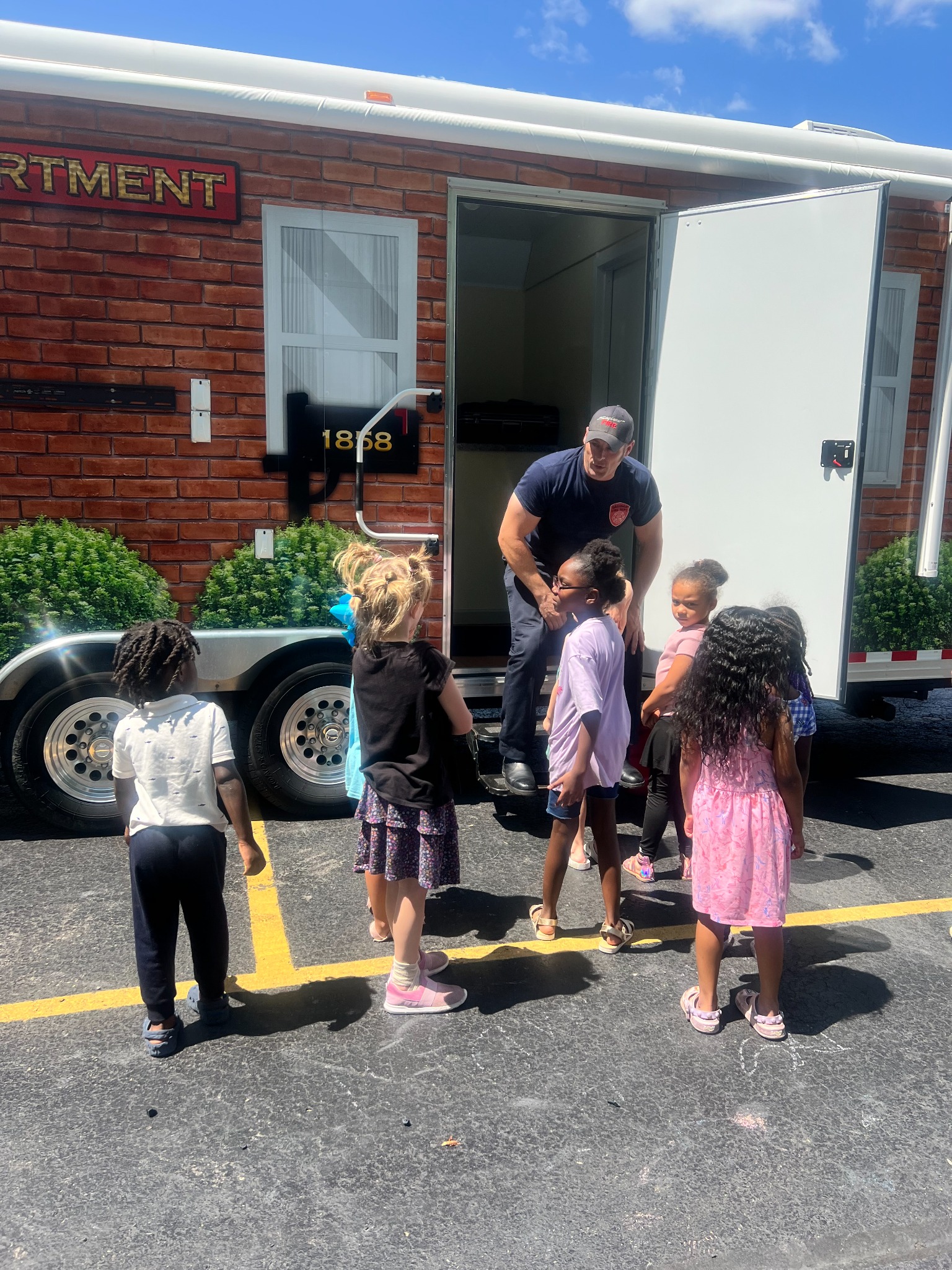 Children learning with a firefighter beside a mobile fire-safety smokehouse